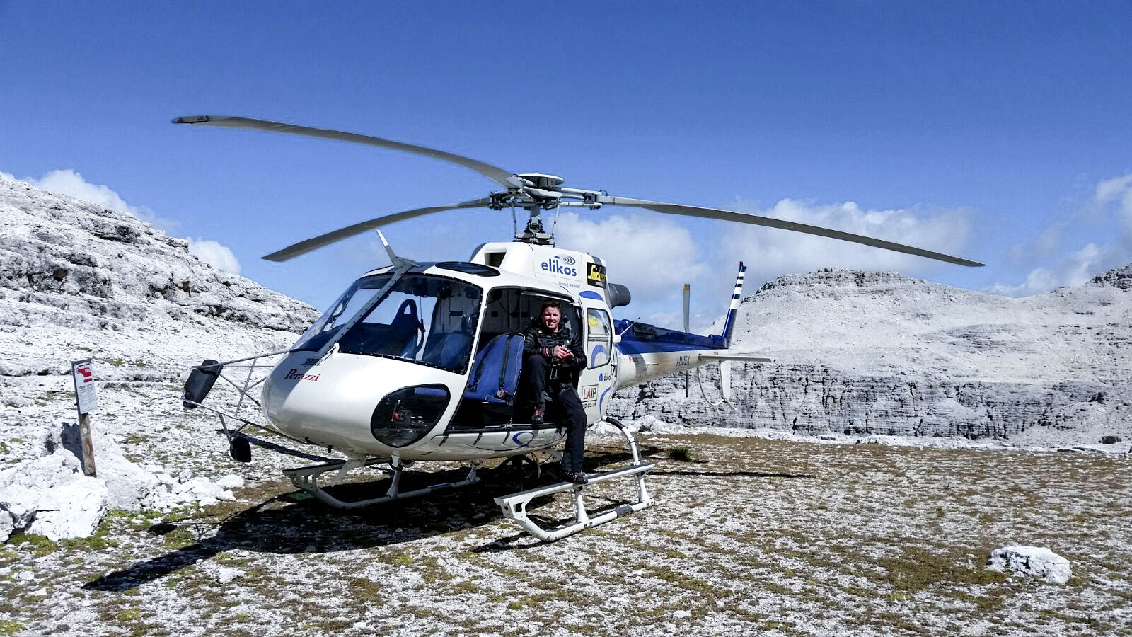 Clear Angle Studios crewmember sitting in the door of a helicopter in front of snowy mountains in Italy, before beginning an aerical enviroment 3d scan capture.