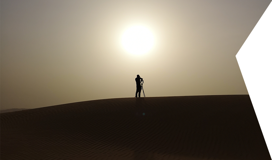 Desert HDRI silhouette. Clear Angle crewmember silhouetted against the sun oon top of a sand dune, setting up a Roundshot to capture an HDRI image.