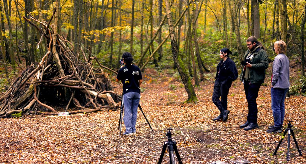 Clear Angle crewmember observing a student from Bucks New University as they are 3D photogrammetry scanning and texturing a structure made of branches in a clearing in the woods.